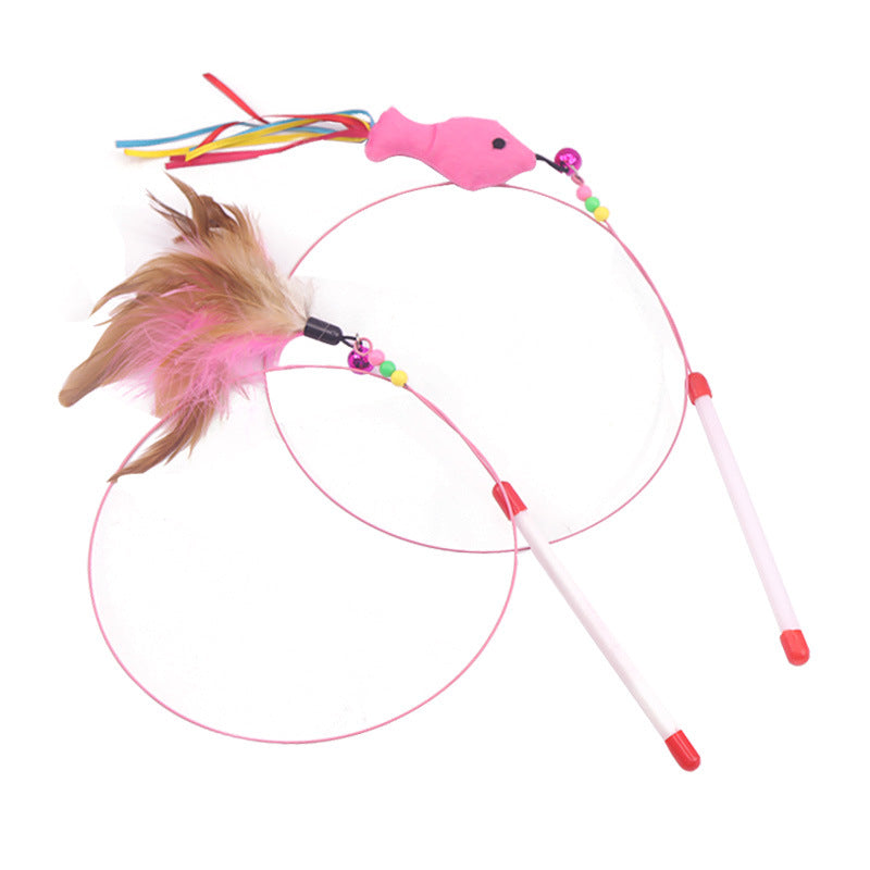 A pink cat toy consisting of two wand-like sticks with thin pink loops, a small pink fish-shaped handle, colorful beads, a brown feather, and multicolored tassels, photographed on a white background.